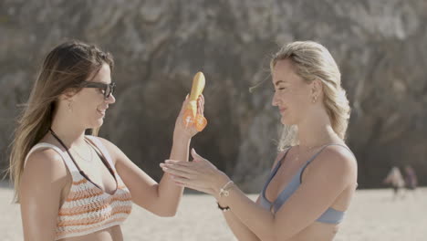 Girl-in-bikini-helping-friend-to-apply-sunscreen-on-shoulders